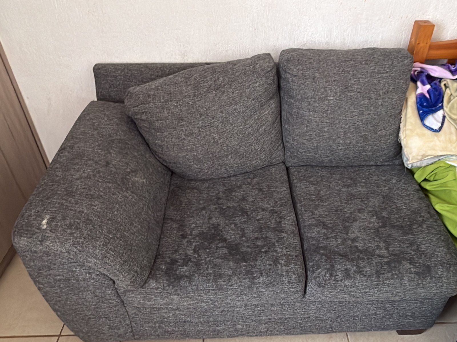 Sofá de tela gris con manchas y el asiento apelmazado, antes del lavado